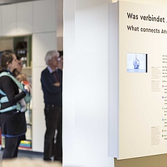 Eine Gruppe, darunter eine Frau mit Kind, steht vor eine Ausstellungswand