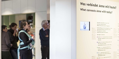 Eine Gruppe, darunter eine Frau mit Kind, steht vor eine Ausstellungswand