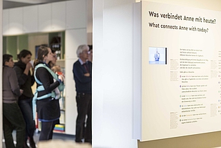 Eine Gruppe, darunter eine Frau mit Kind, steht vor eine Ausstellungswand