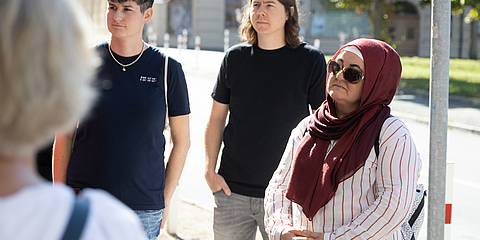 Eine Gruppe von Menschen steht auf einer Straße. Eine Frau trägt einen Hijab.